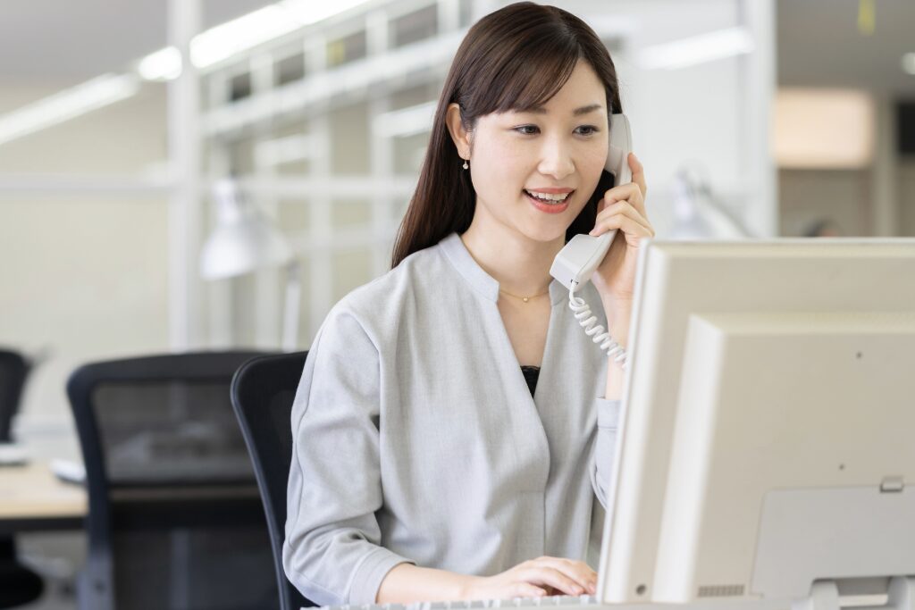 事務員がパソコンの前で電話している様子